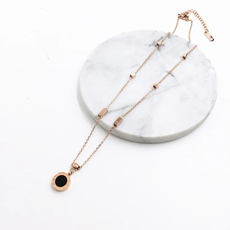 Rose gold necklace with a black pendant on a marble stand