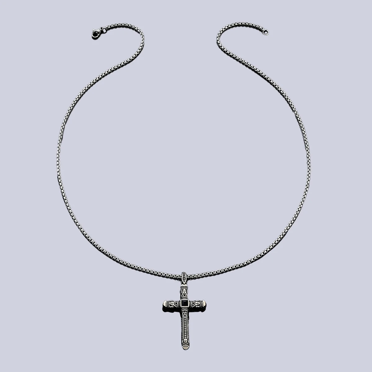 A silver-toned cross pendant necklace with a textured, diamond-like pattern on the cross and a matching chain, displayed against a solid light gray background.