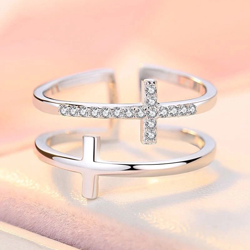 Silver cross-shaped ring on a soft pink background