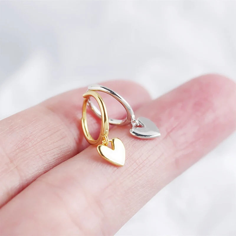 Gold and silver heart-shaped earrings on a hand against a white background