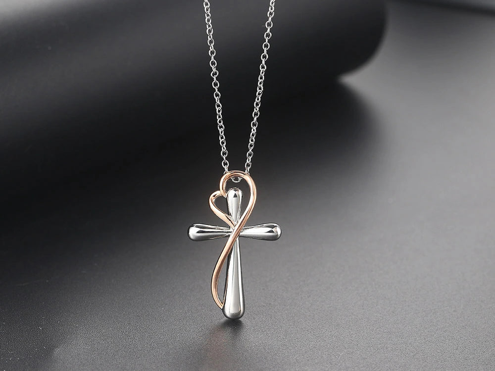 A silver cross pendant necklace with a rose gold infinity loop forming a heart shape at the top, hanging from a silver chain against a dark gray background.