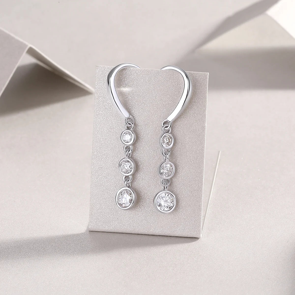 Silver earrings with clear stones on a gray card against a light gray background