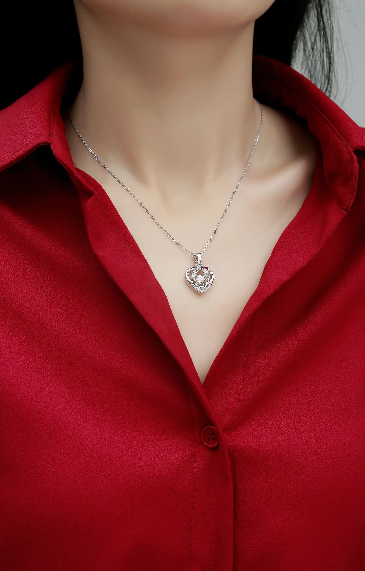 Silver necklace with a heart-shaped pendant worn by a person in a red shirt.