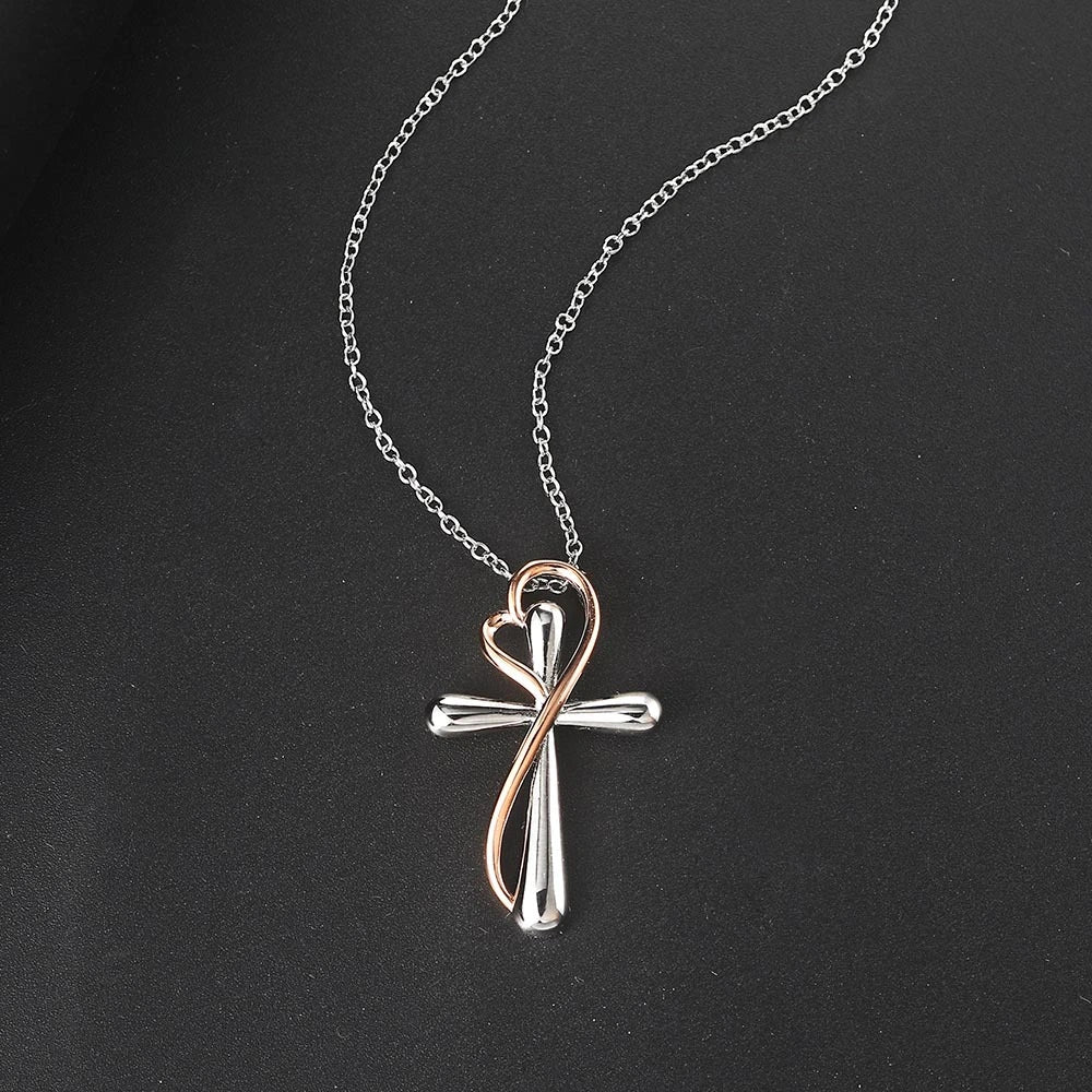 A silver cross pendant necklace with a rose gold infinity loop forming the ankh symbol, displayed on a dark textured background.