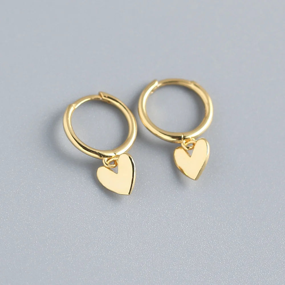 Gold hoop earrings with heart charms on a gray background