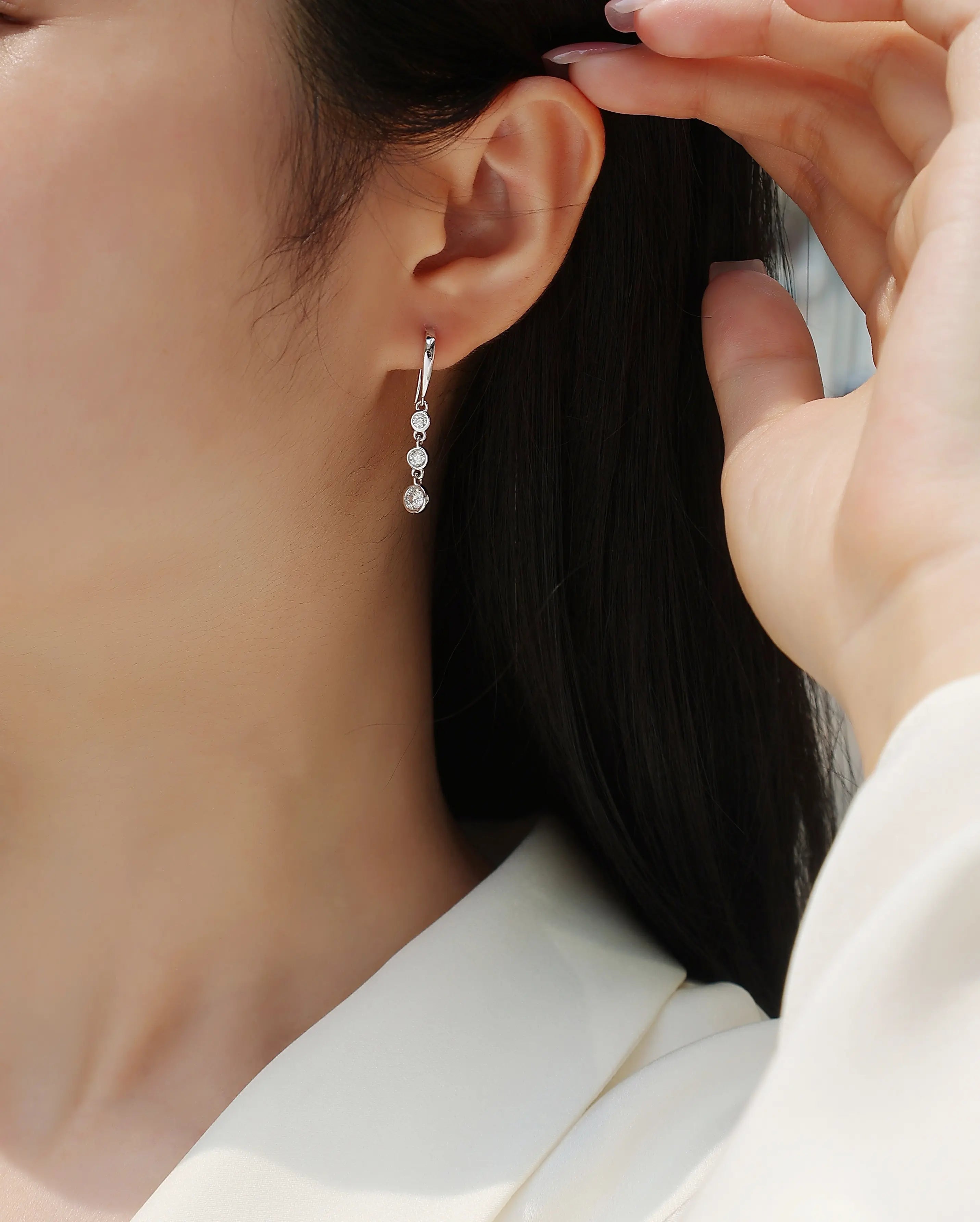 Close-up of a person wearing a silver earring with a hand adjusting it.