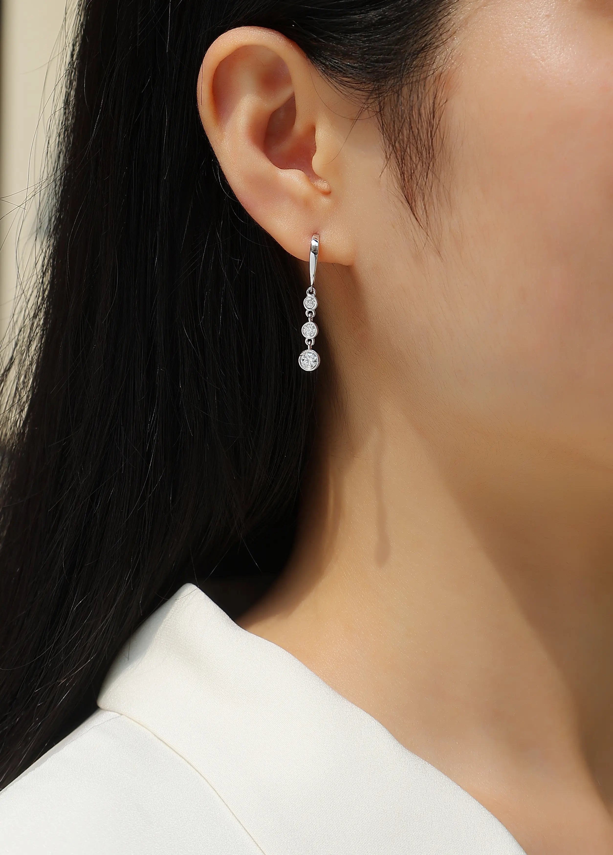 Close-up of a person wearing a silver earring with clear gemstones.